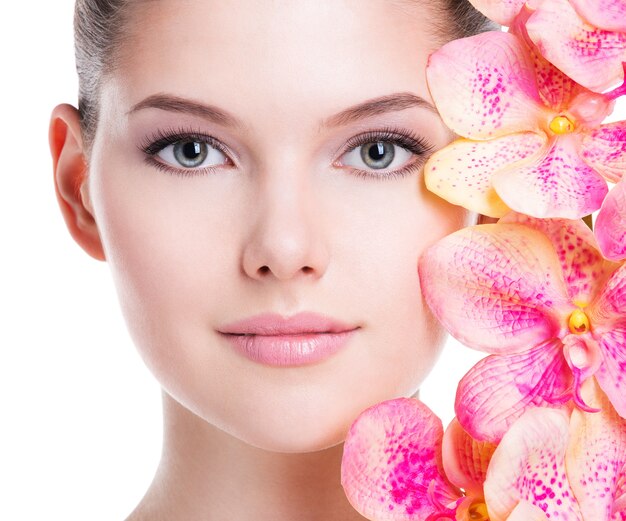 Closeup portrait of beautiful young woman with healthy skin and pink flowers near face - isolated on white.