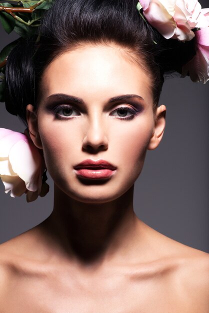 Closeup portrait of beautiful young woman with pink flowers in hair - on a gray background