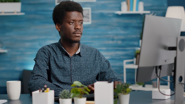 カメラに微笑んで、リビングルームのコンピューターで作業している黒人アフリカ系アメリカ人男性のクローズアップの肖像画。社会的な距離を保ちながら自宅で仕事をしているリモートインターネットオンラインウェブマネージャー