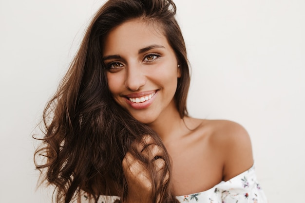 Closeup portrait of charming dark-haired green-eyed tanned woman on white wall