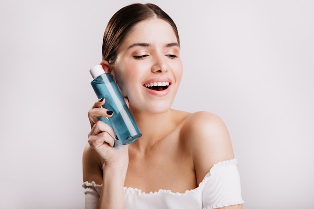 Closeup portrait of cute girl without makeup holding blue bottle with healing tonic for face skin.