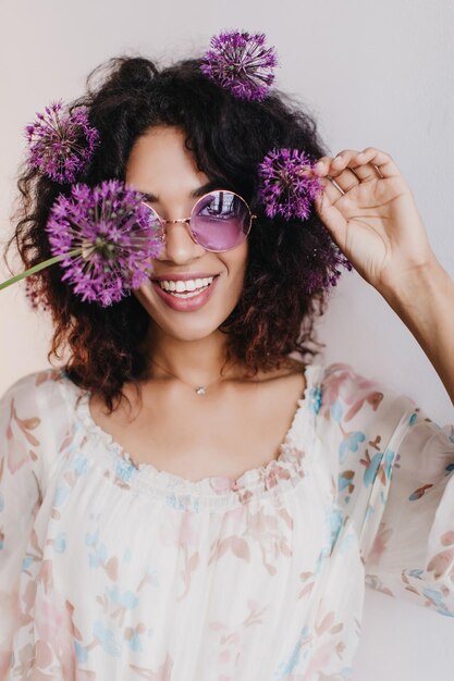 Closeup portrait of excited african girl playfully posing with flowers Indoor shot of ecstatic black young woman wears glasses