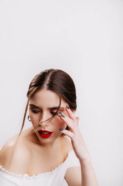 Closeup portrait of girl with perfect skin tone and red lips playing hair on white wall.