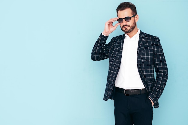 Closeup portrait of handsome confident stylish hipster lambersexual model Sexy modern man dressed in black elegant suit Fashion male posing in studio blue wall