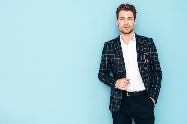 Closeup portrait of handsome confident stylish hipster lambersexual model Sexy modern man dressed in black elegant suit Fashion male posing in studio blue wall