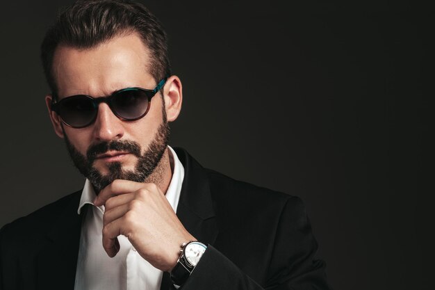 Closeup portrait of handsome confident stylish hipster lambersexual model Sexy modern man dressed in elegant black suit Fashion male posing in studio on dark background In sunglasses