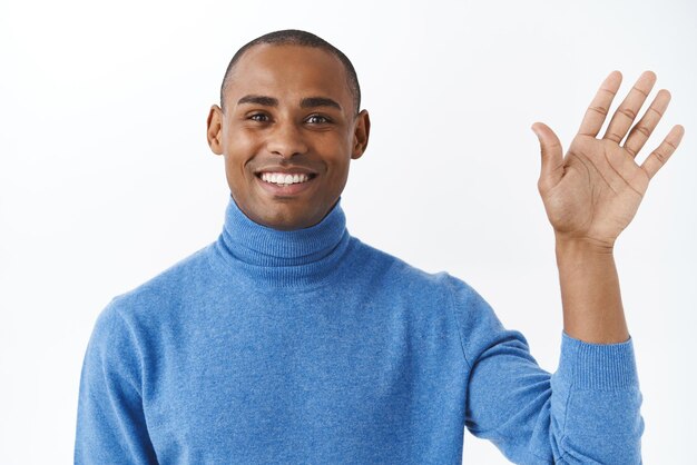 Closeup portrait of happy friendlylooking handsome african american waving hand in hello or goodbye say hi to friend pleased to meet person standing white background upbeat