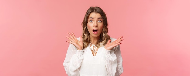 Free photo closeup portrait of impressed and surprised blond girl hear something stunning and impressive happened drop jaw spread hands sideways look astonished with news pink background