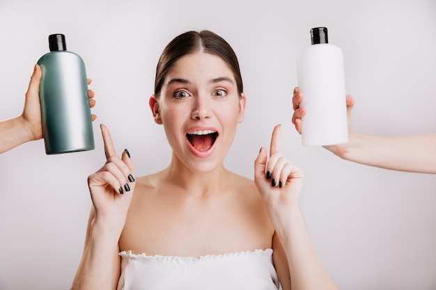 Closeup portrait of joyful girl posing without makeup on white wall. woman chose which shampoo is best to use.