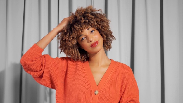 Closeup portrait of mixed race black woman with textured curly afro hair in bright orange jacket with natural makeup for dark skin tones