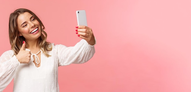 Портрет крупным планом стильного красивого блогера красоты, записывающего видео на смартфон, делающего селфи, показывающего большой палец на камеру мобильного телефона, улыбающегося, довольного, рекомендую место подписчикам Premium Фотографии