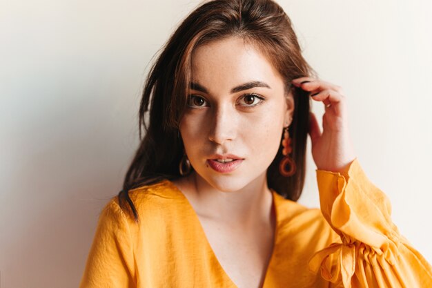 Closeup portrait of pensive brown-eyed girl in yellow blouse on posing gray wall.