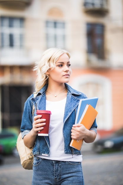 Free photo closeup portrait of pretty blonde girl student with a lot of notebooks dressed up in jeans