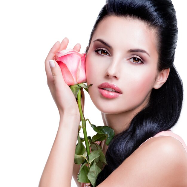 Closeup portrait of sensual beautiful woman with pink rose on white wall.