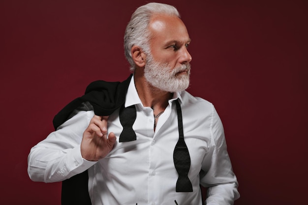 Free photo closeup portrait of white haired man in shirt stylish bearded guy with tattoos in light shirt looking away on burgundy background