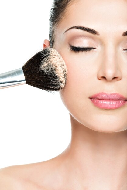 Closeup portrait of a woman  applying dry cosmetic tonal foundation  on the face using makeup brush.