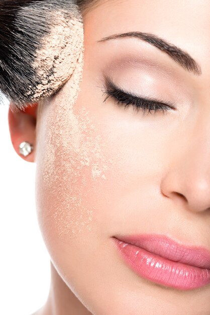 化粧ブラシを使用して顔にドライ化粧品の色調のファンデーションを適用する女性のクローズアップの肖像画。