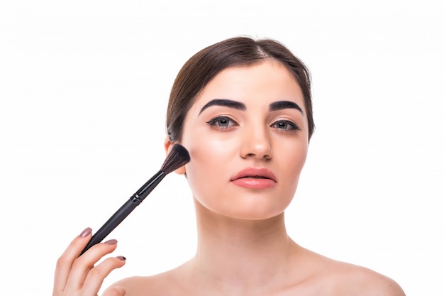 Closeup portrait of a woman applying dry cosmetic tonal foundation on the face using makeup brush.