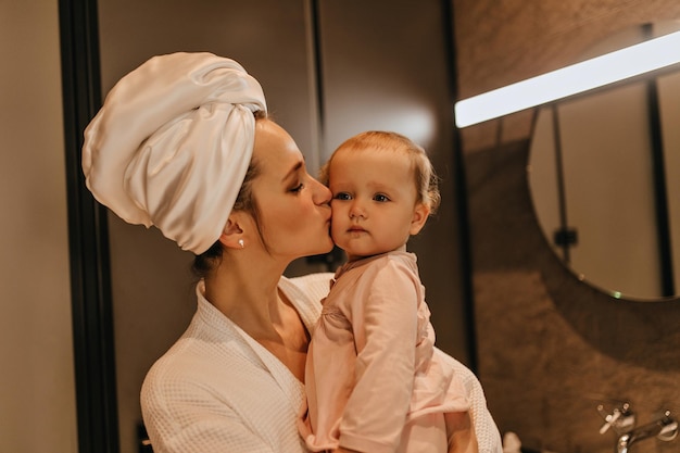 Closeup portrait of woman in towel after shower kissing fairhaired little daughter