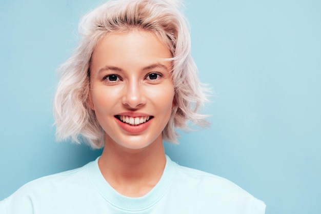 Closeup portrait of young beautiful smiling female in trendy summer clothes Sexy carefree woman posing near blue wall in studio Positive blond model having fun Cheerful and happy