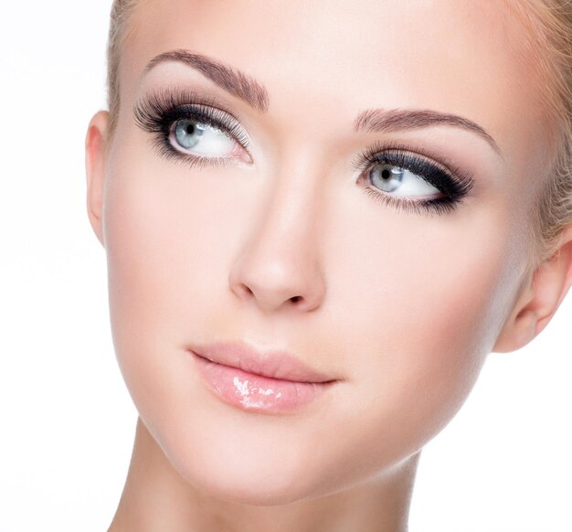 Closeup portrait of young beautiful white woman with long false eyelashes  over white wall