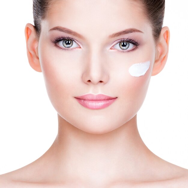 Closeup portrait of young woman applying cream on her pretty face over white background.