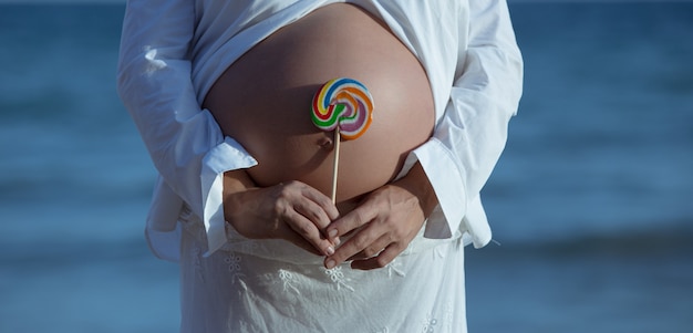 Free photo closeup of a pregnant female holding a lollipop near her belly under the sunlight