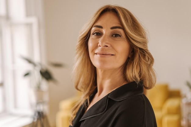 Closeup of pretty middleaged caucasian lady in black shirt with smile on her face looks at camera on blurred background