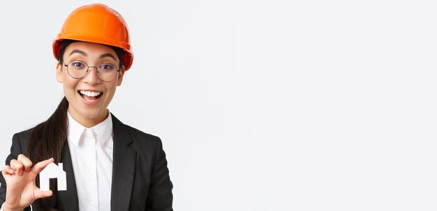 Closeup of professional broker in safety helmet and business suit selling homes Cheerful architect showing minuature of house and smiling working over new design or construction white background