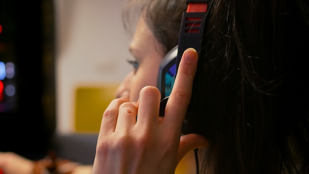 Closeup of professional gamer wearing headset and talking with other players into microphone during esport tournament. Player sitting on gaming chair playing space shooter game using RGB equipment