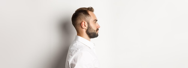 Closeup profile shot of handsome bearded man looking left standing against white background