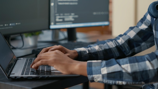 Closeup of programer hands typing machine learning code on laptop keyboard in front of computer screens with programming interface. System engineer writing algorithm for online cloud computing.