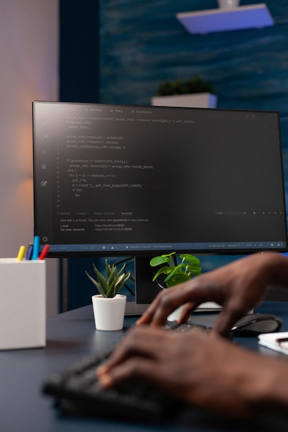 自宅から離れた場所で作業しているコンピューターでウェブサイトのスクリプトを入力するプログラマーの男の手のクローズアップ。ネットワークセキュリティシステムを使用してバイナリコードをプログラミングするアフリカ系アメリカ人のハッカー労働者。コーディングの概念