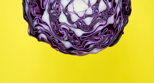 Макрофотография фиолетовой круглой капусты разрезать пополам на желтом фоне