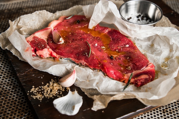 Closeup of raw meat with seasonings and herbs on a wooden board