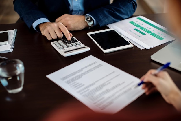 Closeup of real estate agent using calculator while his client is signing a contract