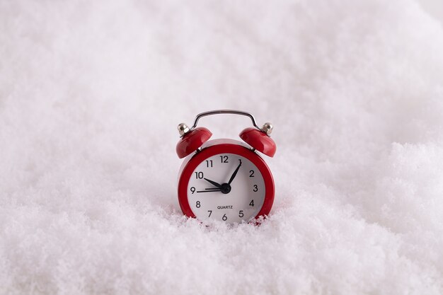 雪の中で赤い目覚まし時計のクローズアップ、新年までの時間を数える時計
