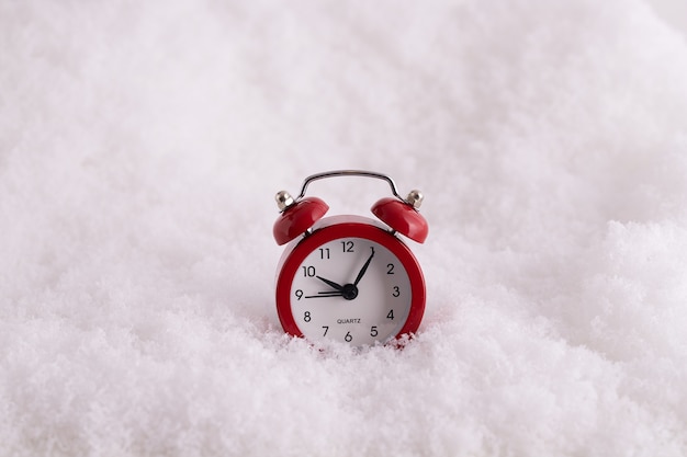 Крупным планом красный будильник на снегу, часы, отсчитывающие время до Нового года