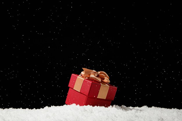 Closeup of a red Christmas gift box on fake snow against a black scene