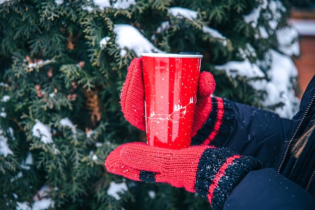 Closeup of a red thermal cup in hands in red mittens
