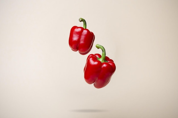 Closeup of ripe red bell peppers falling on a beige surface