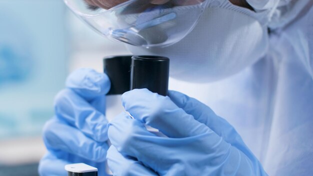 Closeup of scientist researcher doctor looking into medical microscope analyzing virus sample working at coronavirus vaccine development in microbiology hospital laboratory. Medicine concept