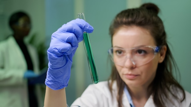 DNA 샘플이 있는 시험관을 보고 있는 과학자 여성의 근접 촬영