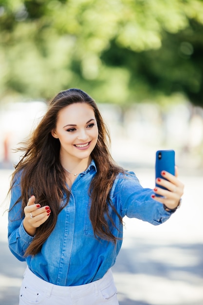 クローズアップselfie-街で長い髪型と真っ白な笑顔のサングラスで魅力的な女の子の肖像画の学生。