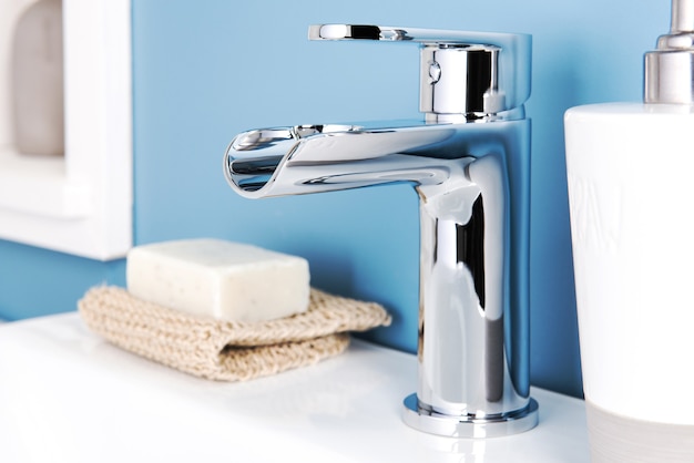 Closeup of a shiny modern faucet and soap dispenser in a bathroom