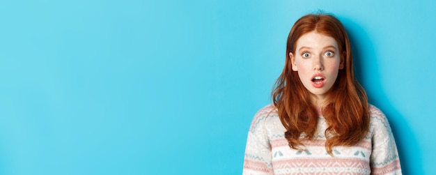 Closeup of shocked redhead girl drop jaw in awe staring with amazement at camera standing against bl