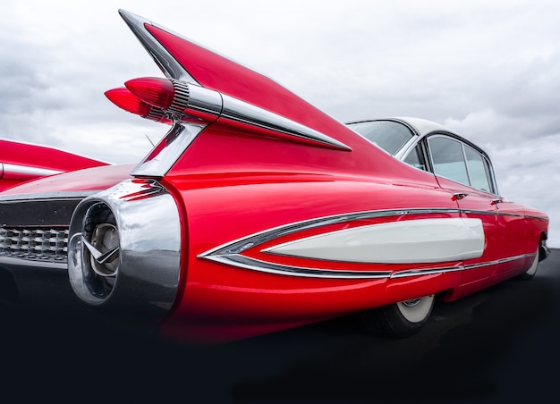 Closeup shot of the back part of a red car under a sky full of clouds