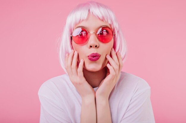 Closeup shot of beautiful goodhumoured woman in pink sunglasses Indoor photo of european trendy girl wears peruke