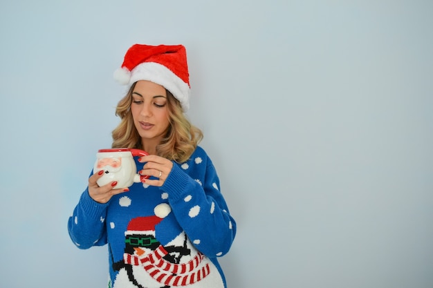 Closeup shot of a beautiful young lady wearing a christmas dress and hat holding a santa cup