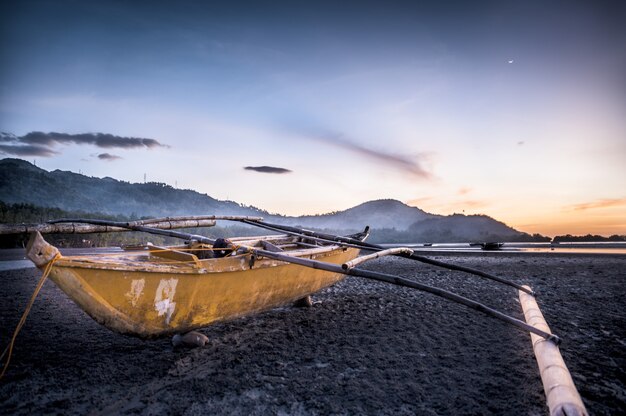 Closeup shot of a boat on the shore with mountains and a beautiful sky in the